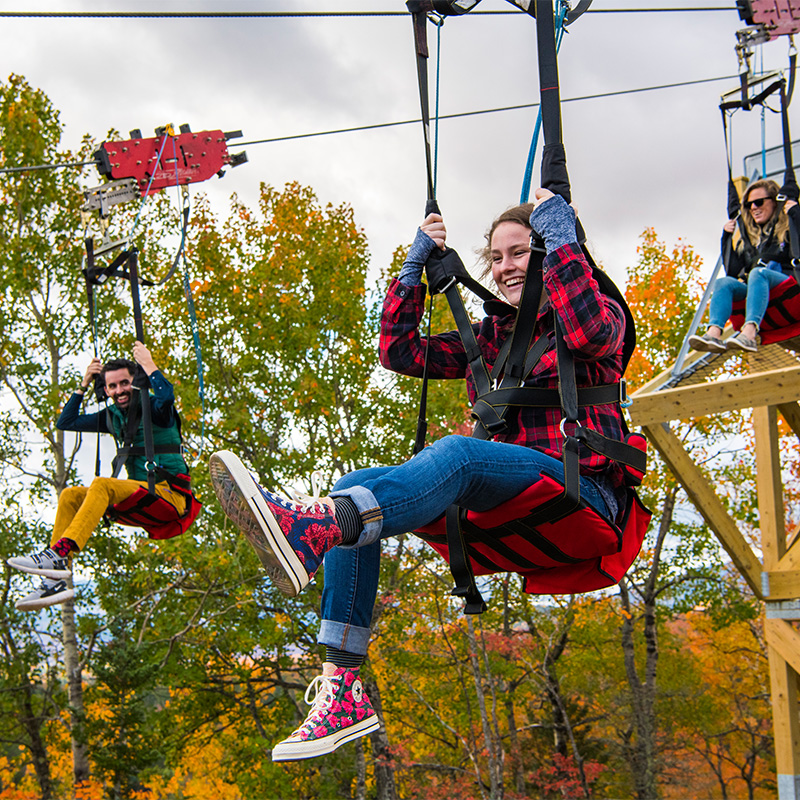 Three people get ready to zipline during peak foliage at the ski jumps.