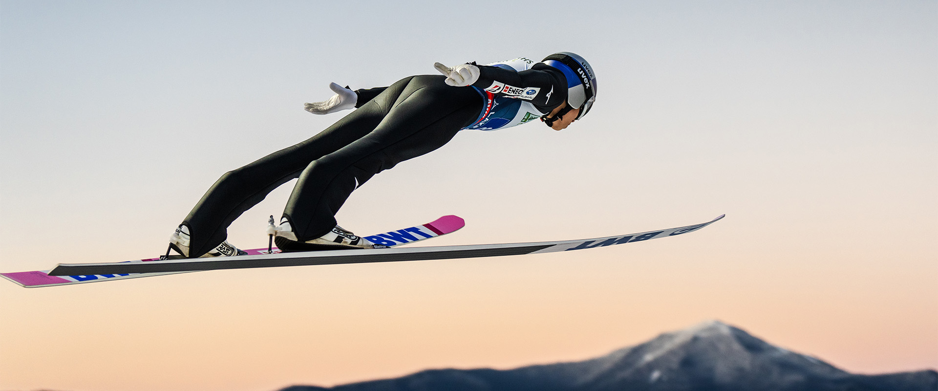 A ski jumper flies through the air with whiteface mountain in the background.